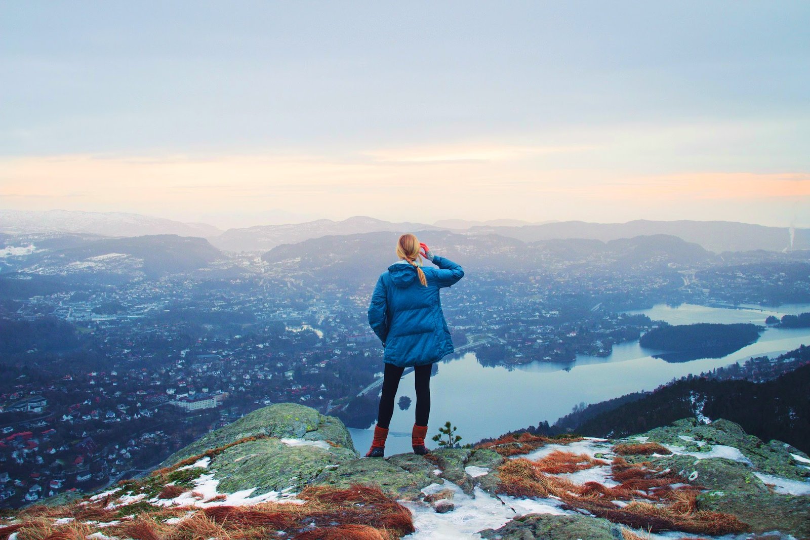 Foto einer Frau auf einem Berg, die Richtung Horizont ins Tal blickt, unten ein Fluss, am Horizont Berge
